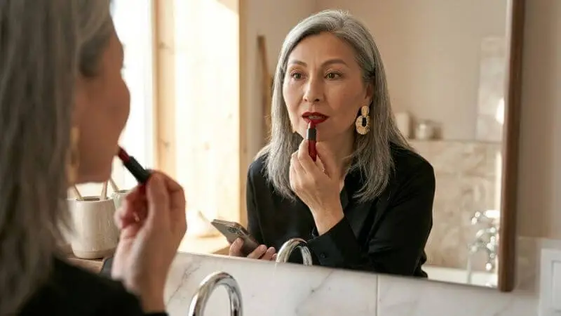 Mulher madura passando batom vermelho no espelho, truque final para look chique de festa de última hora